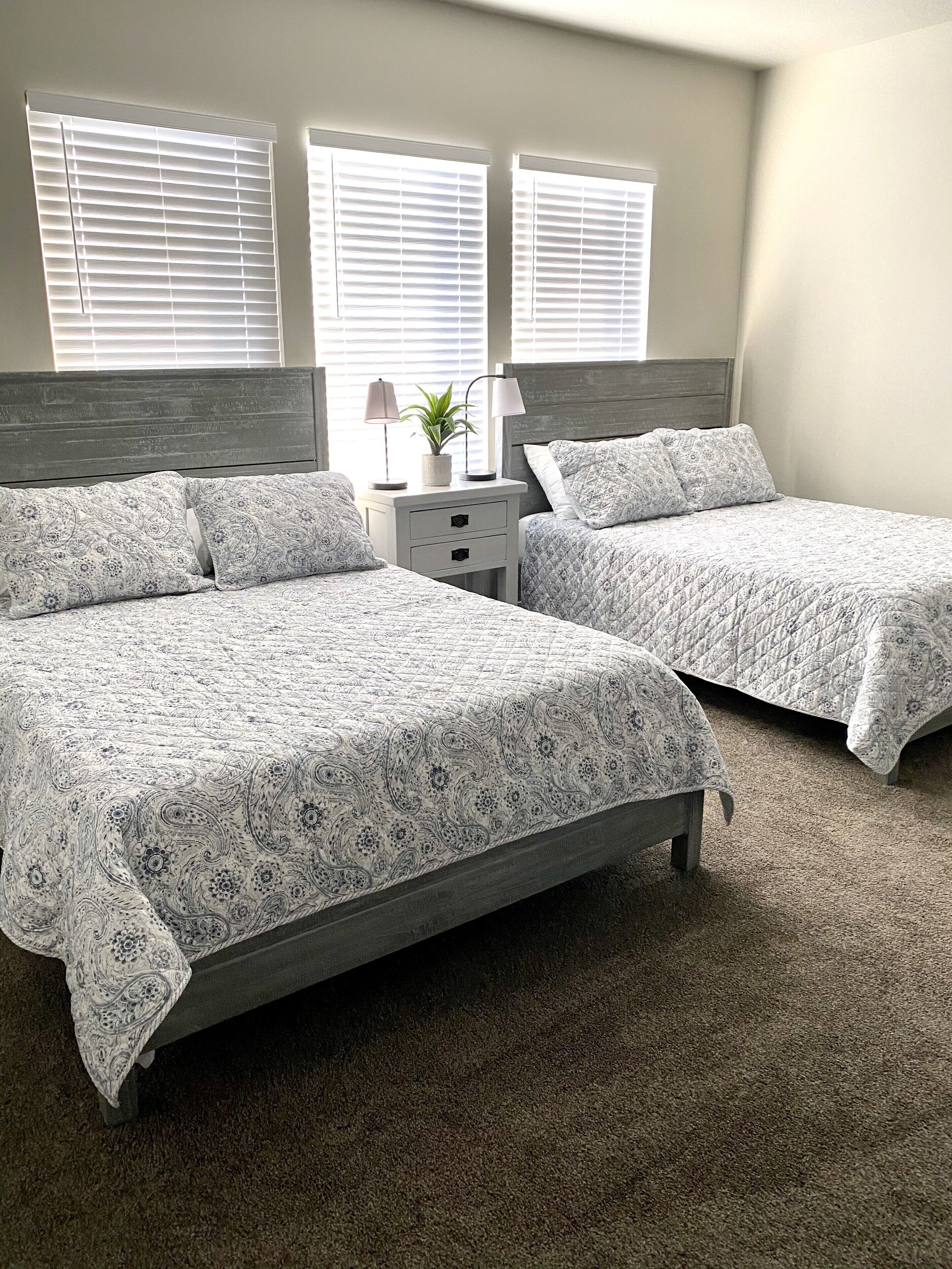 A bedroom with two beds, a nightstand, and a potted plant.