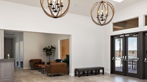 A spacious living area with a high ceiling, two chandeliers, a seating arrangement with sofas and a bench, and a view through a glass door to an outdoor area. - NEW🌟Spacious, Zion Village 7BD/6BA, Sleeps 32, Pool, Lazy River, View  (Hurricane)