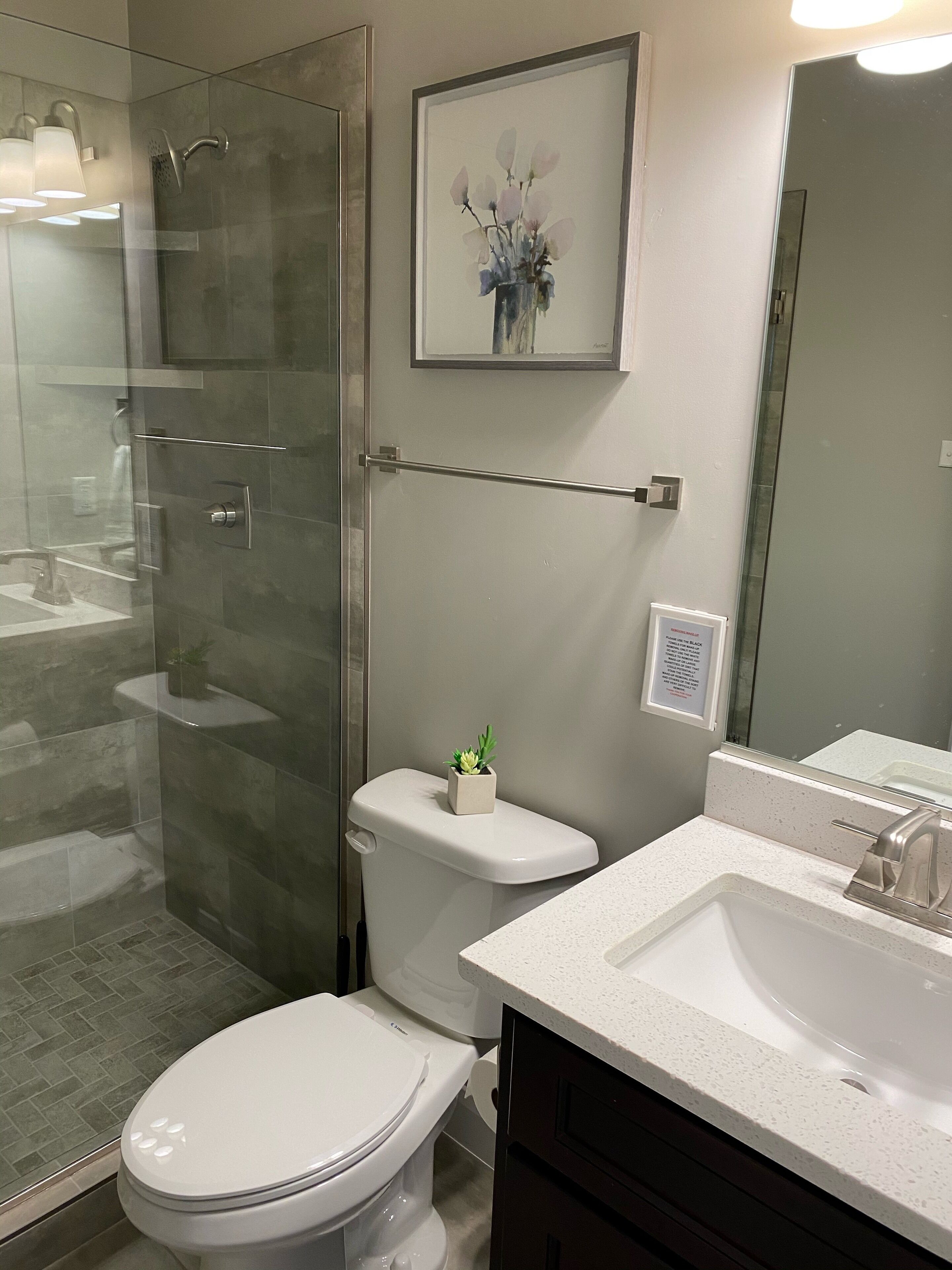 Een moderne badkamer met een douchecabine van glas, een toilet, een wastafel en een kunstwerk in een lijst aan de muur.