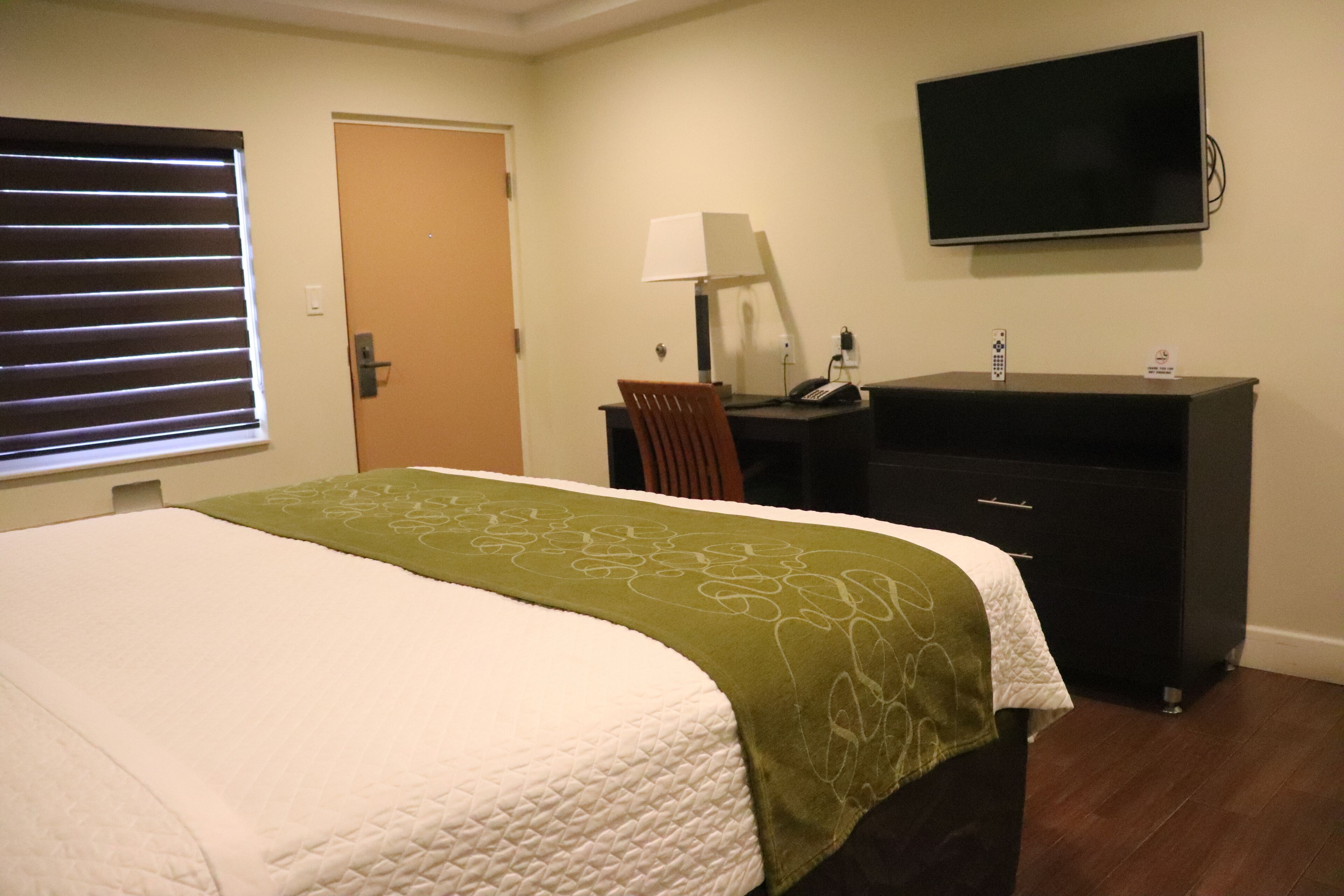 A hotel room with a bed, a desk, a chair, a TV, and a window with blinds.
