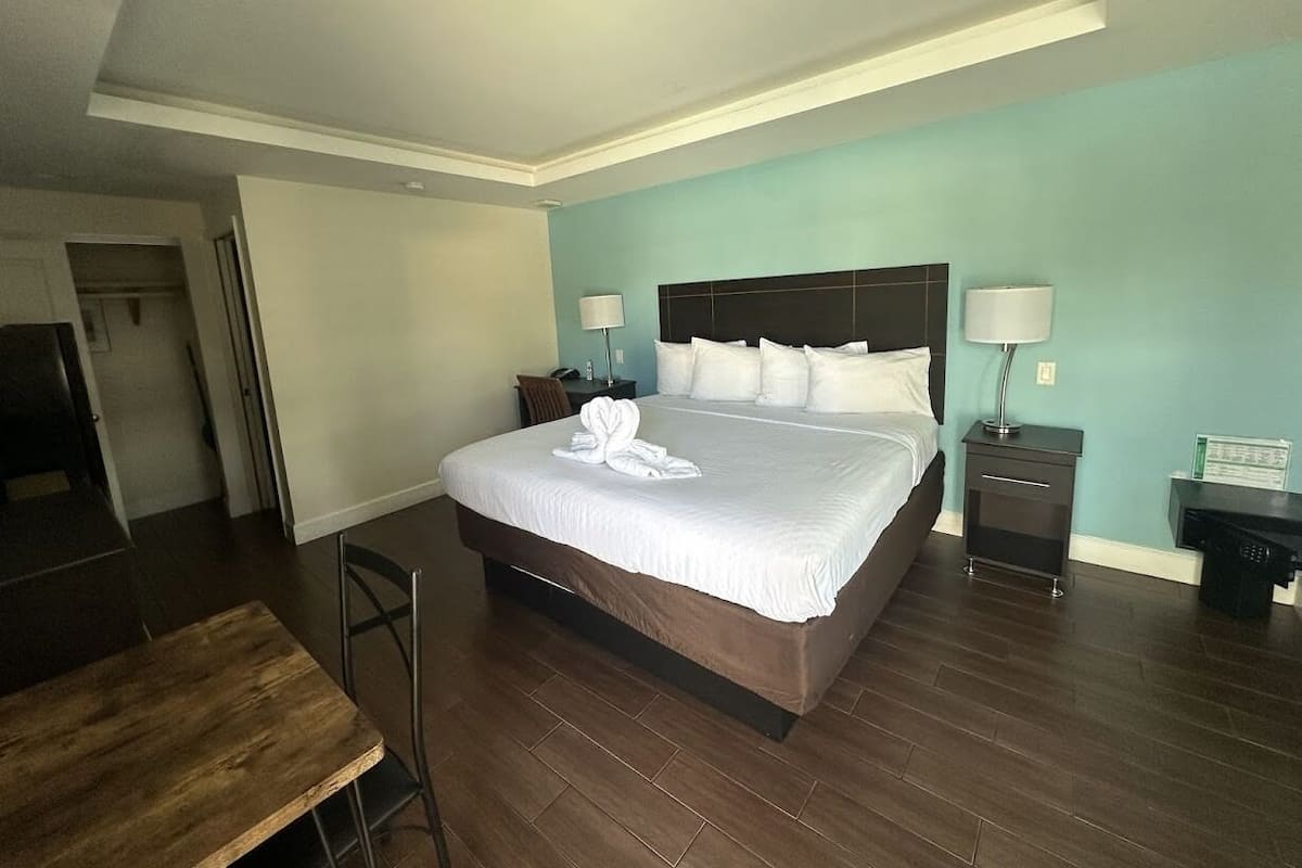 Una habitación de hotel con una cama grande, un escritorio de madera y una mesita de noche con lámpara.