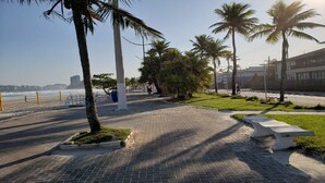 A paved walkway with palm trees, a bench, and a view of the beach and ocean.