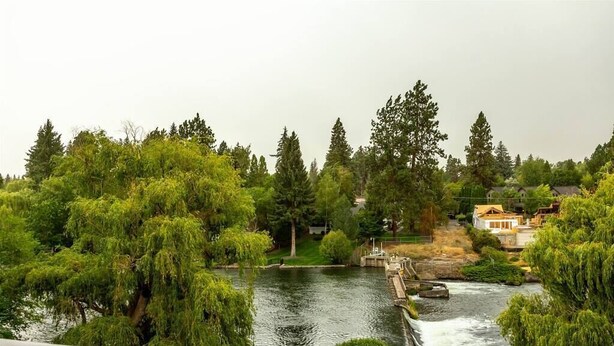 Une rivière traversée par un pont, entourée d’une végétation luxuriante et avec des maisons en arrière-plan.