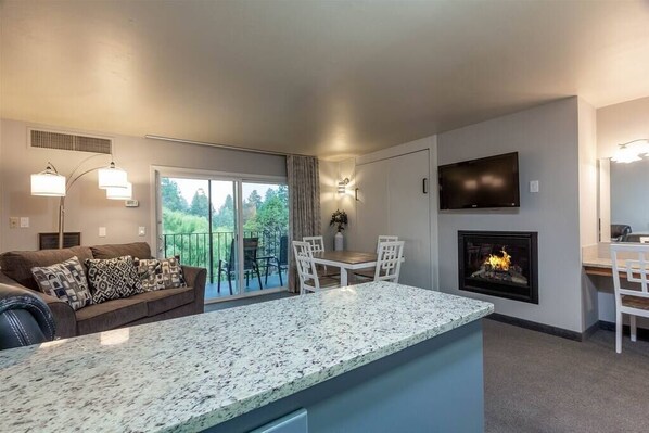 A modern living room with a fireplace, a dining area, and a large window overlooking a balcony.