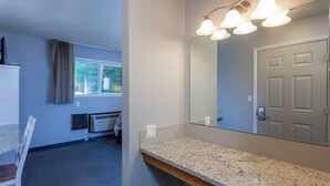 Une salle de bain avec un comptoir en granit, un miroir et un luminaire au plafond.