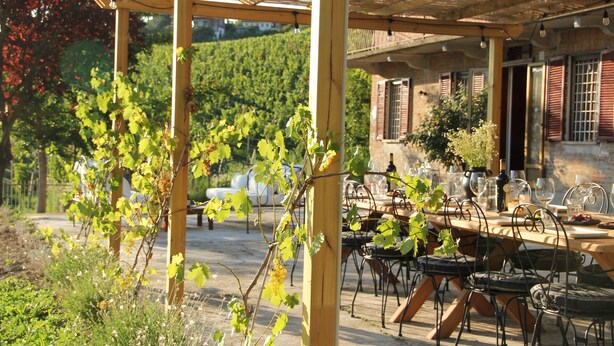 Un espacio de comedor al aire libre cubierto, con una mesa dispuesta para seis personas, rodeado de sillas metálicas.