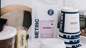 Una mesa blanca con una bolsa blanca etiquetada 'METRIC', un recipiente blanco con la marca 'METRIC', una taza blanca y un plato blanco.