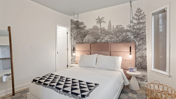 Un dormitorio con cama, mesita de noche, un mural en la pared, una ventana y una puerta.