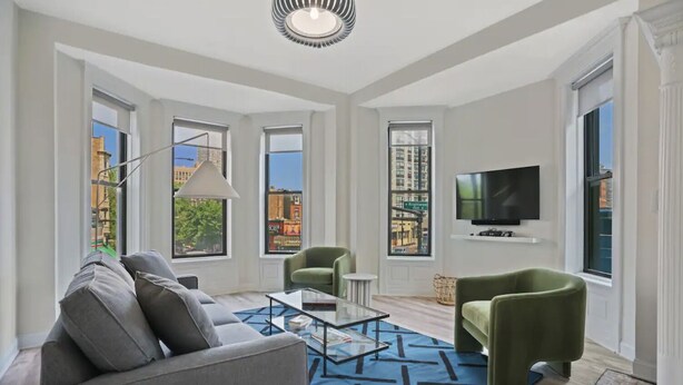Una sala de estar moderna con sofá, sillones, una mesa de centro, televisor y ventanas grandes con vistas a la ciudad.