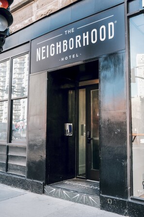 El exterior del Hotel The Neighborhood, con fachada negra, amplias ventanas y una entrada visible.