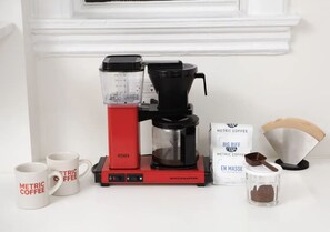 A coffee maker with a scale, two coffee mugs, a bag of coffee, and a scoop.