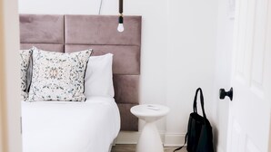 Une chambre à coucher bien rangée, avec un lit, une table de chevet et un petit tabouret.
