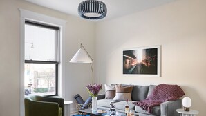 Un salon moderne avec un canapé, des fauteuils verts, une table basse et une grande fenêtre.