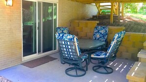 An outdoor patio with a table and four chairs, a sliding glass door, and a brick wall. - Comfortable Apartment in Northwest Omaha (Omaha)