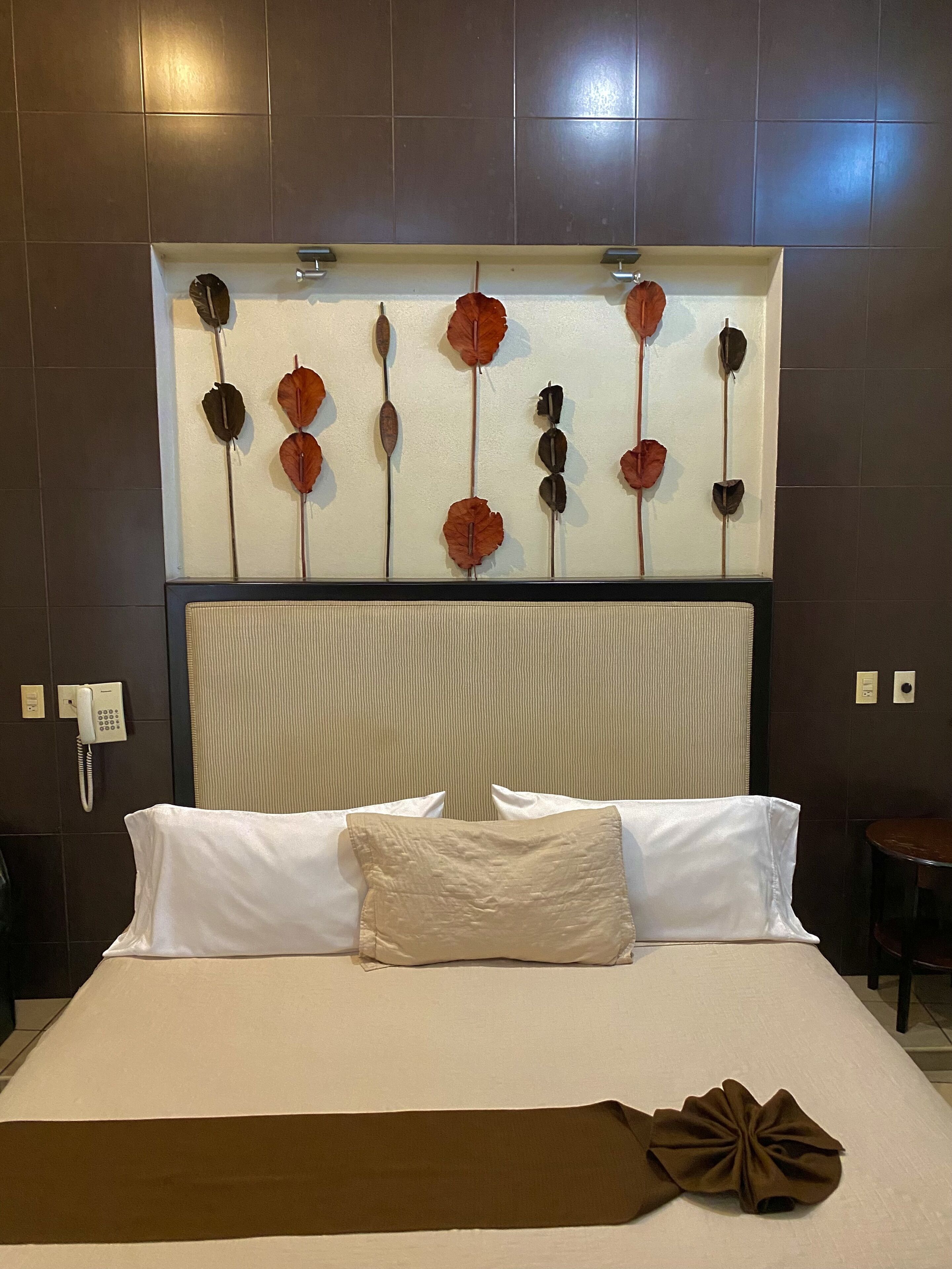 A hotel room with a large bed, white bedding, a decorative wall art piece above the bed, a telephone, and a small table.