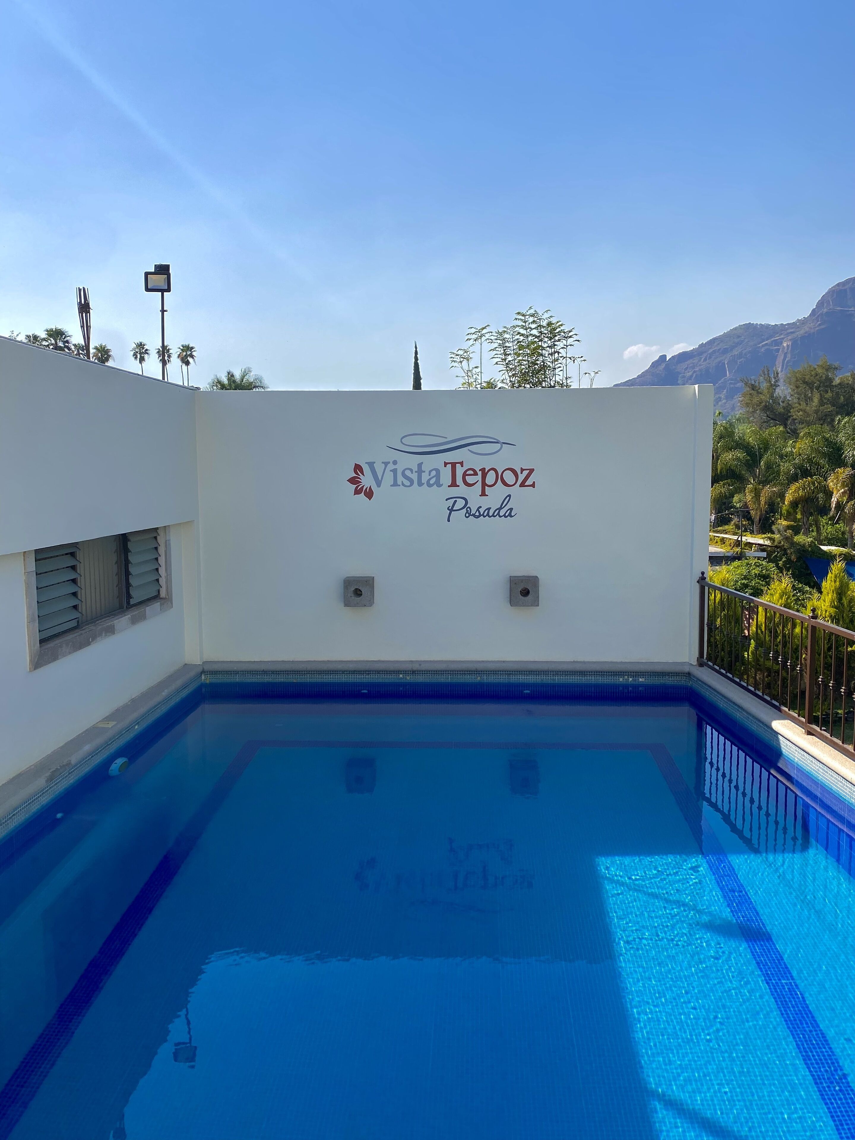 A swimming pool with a sign reading "Vista Tepoz Posada" and a view of mountains and trees in the background.
