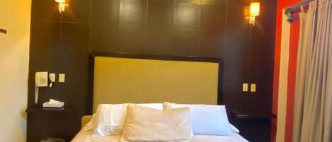 A hotel room with a large bed, a headboard, two bedside tables, and a nightstand.