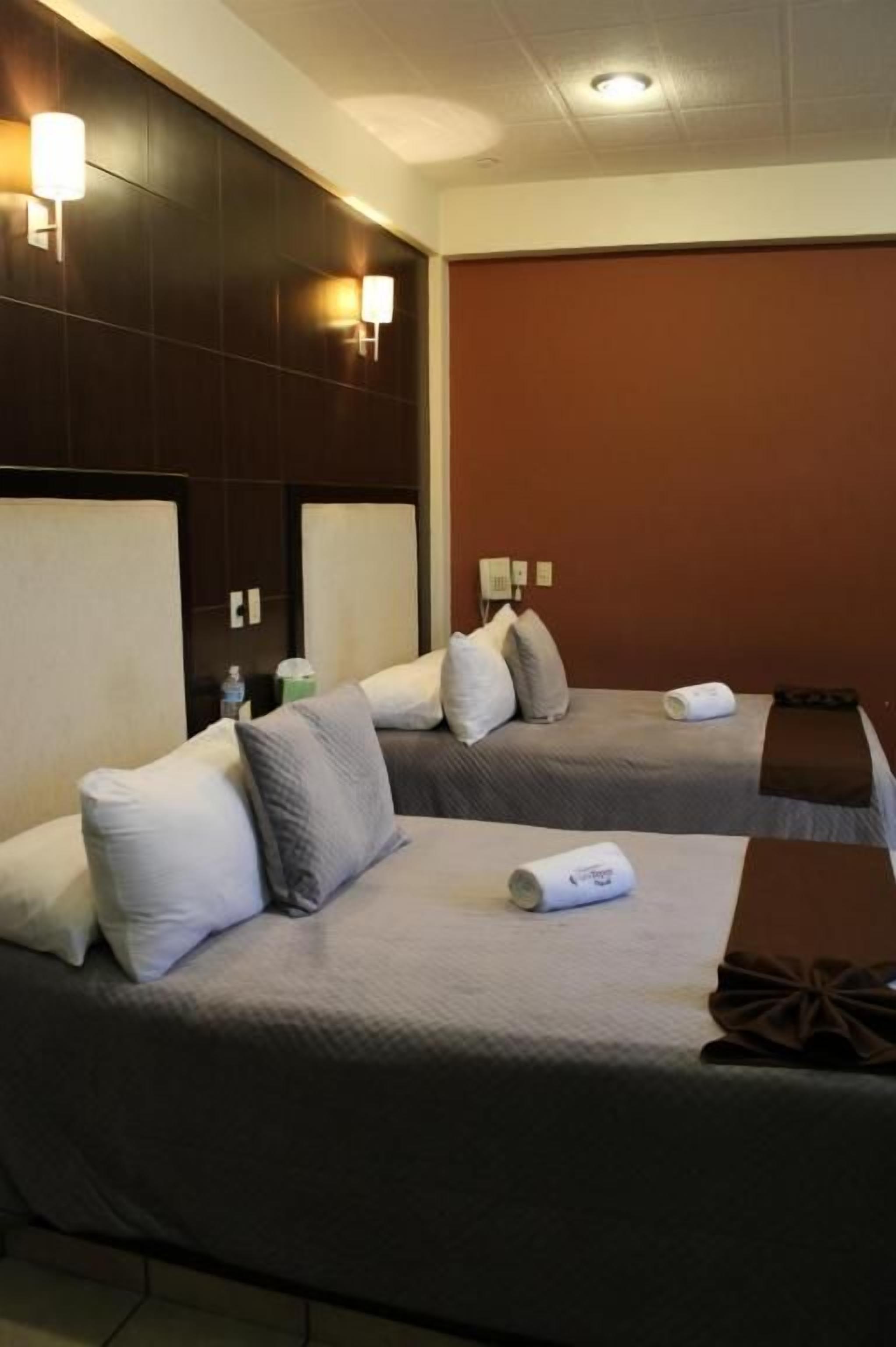 A hotel room with two beds, each with a pillow and a rolled towel.