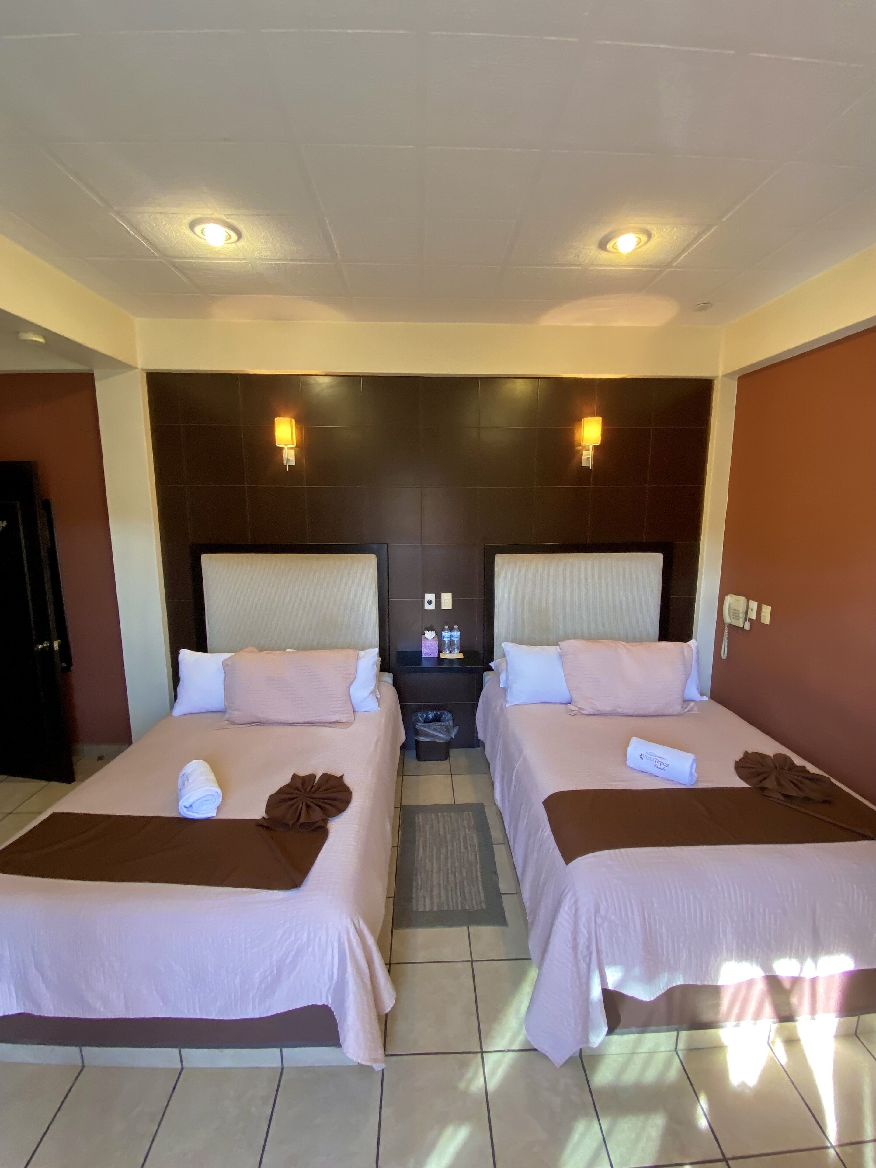 Ein Hotelzimmer mit zwei Betten, einem Nachttisch und einem an der Wand befestigten Telefon.