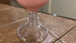A pink smoothie in a glass with a cherry garnish on a tiled surface. - Posada Vista Tepoz (Tepoztlán)