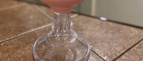 Ein rosa Smoothie im Glas mit einer Kirsche als Dekoration auf einer gefliesten Oberfläche.