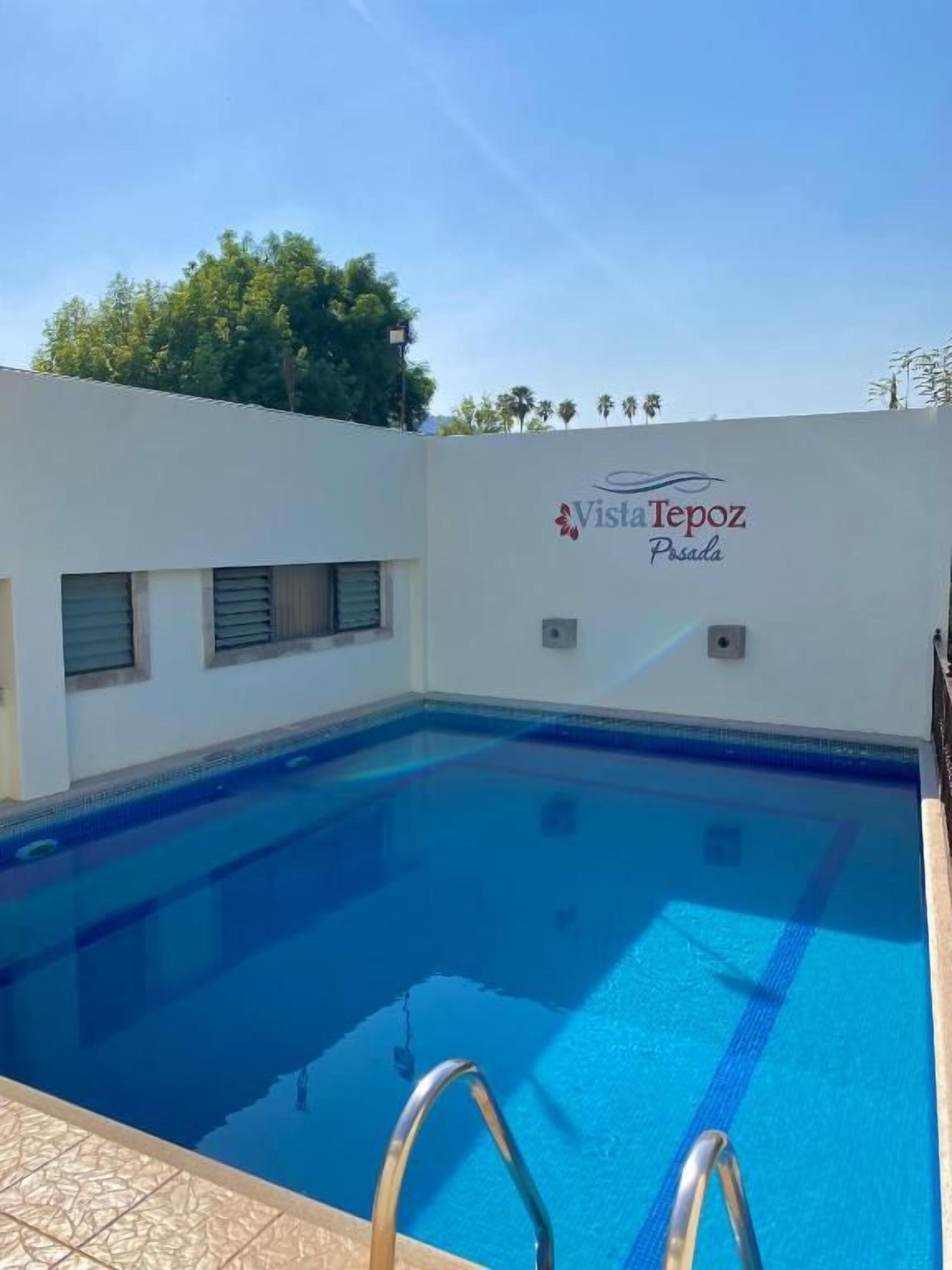 Una piscina con superficie de agua azul cristalina, una escalera de metal y una pared con el texto 'Vista Repoz Pilsen'.