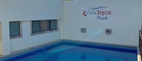 Una piscina con superficie de agua azul cristalina, una escalera de metal y una pared con el texto 'Vista Repoz Pilsen'.