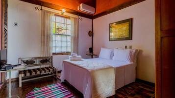 A bedroom with a bed, a desk, a chair, a window with curtains, and a wall-mounted air conditioner.