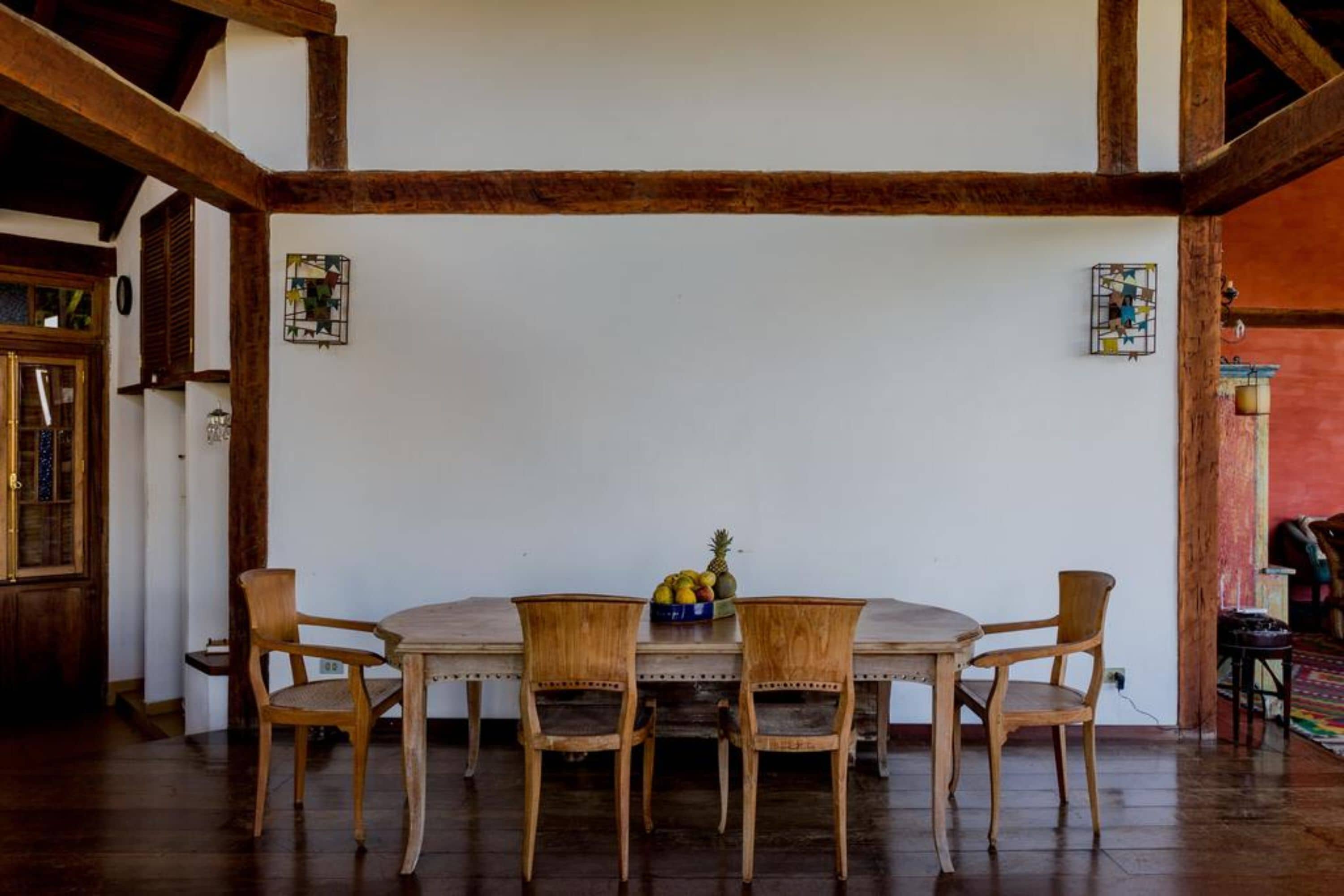 Un comedor con una mesa y sillas de madera, un frutero y una ventana con contraventanas de madera.