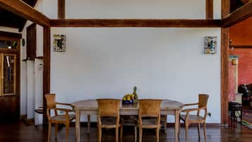 Un comedor con una mesa y sillas de madera, un frutero y una ventana con contraventanas de madera.