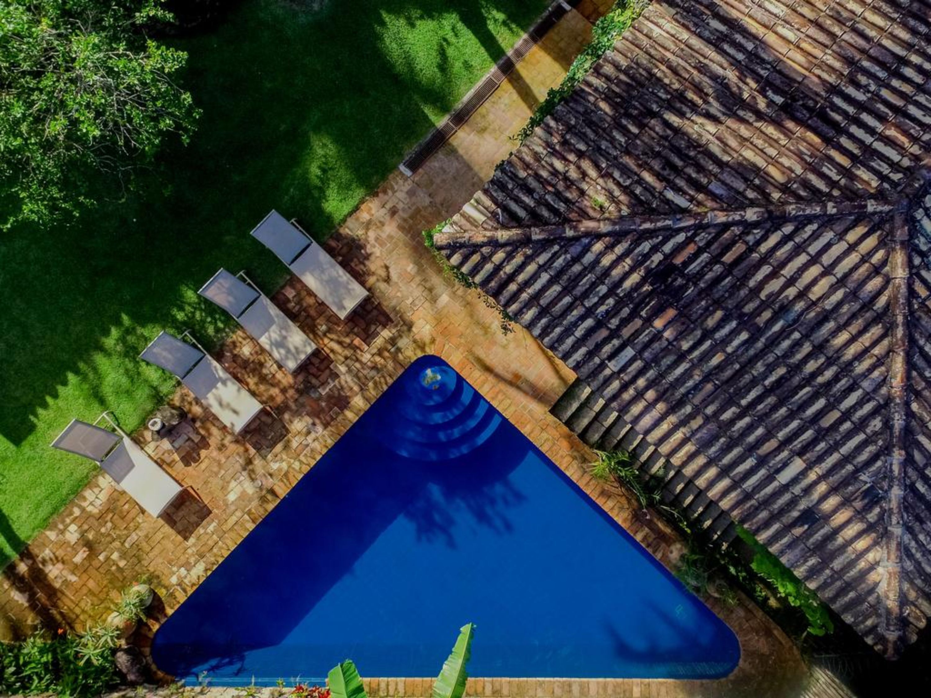 An aerial view of a swimming pool with a thatched roof structure, surrounded by a grassy area and a paved walkway.