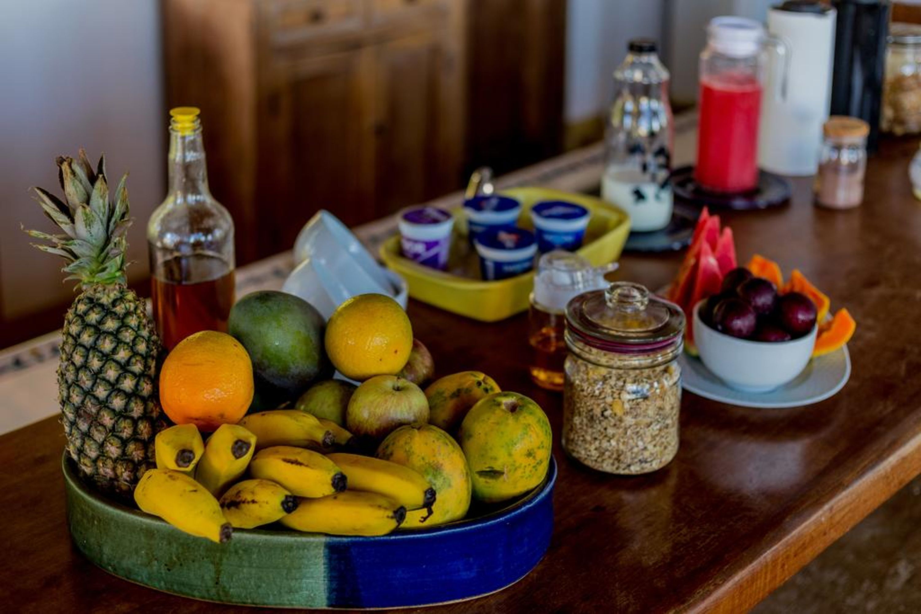 En fruktskål med bananer, äpplen och en ananas på ett träbord.