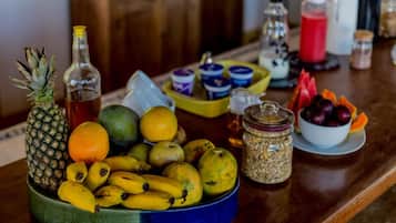 En fruktskål med bananer, äpplen och en ananas på ett träbord.