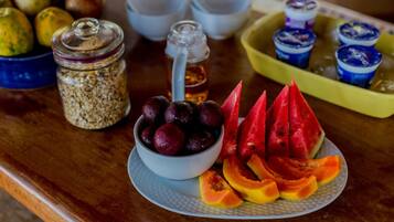 A wooden table with a bowl of cherries, sliced watermelon, and papaya. There are also jars of nuts and a container of honey.