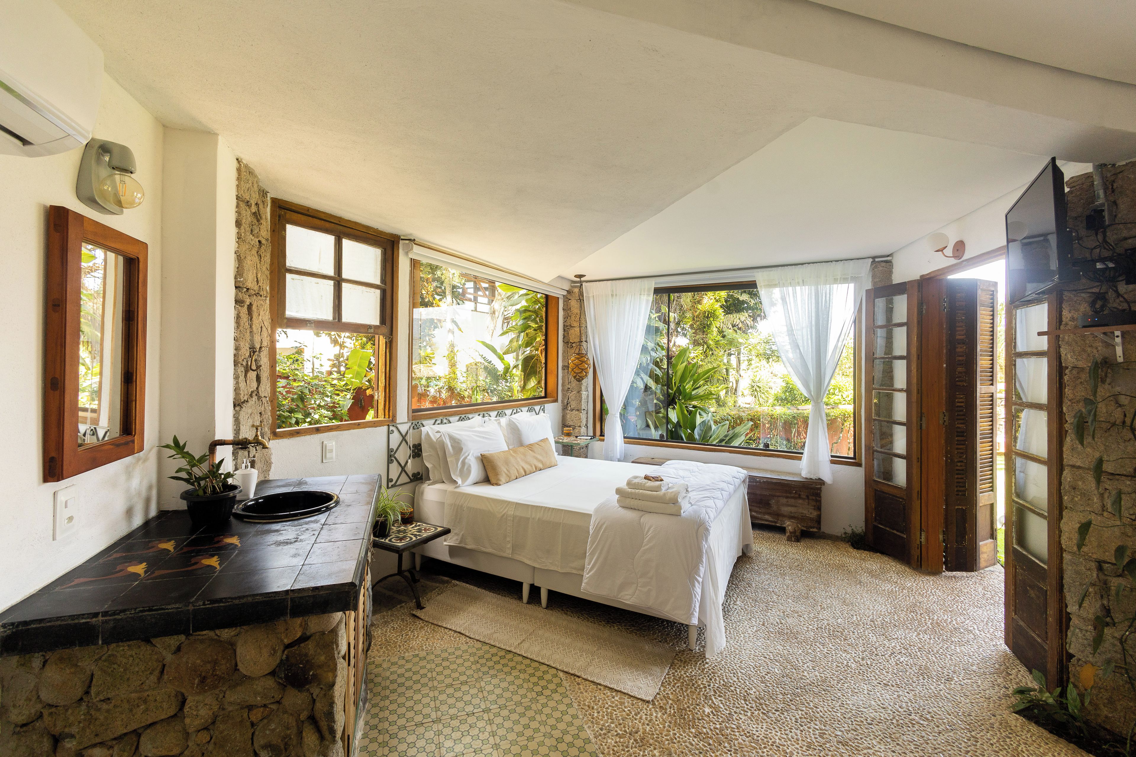 Un dormitorio con cama, lavamanos y ventana con vistas a la vegetación.