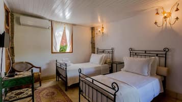 Quarto com duas camas de solteiro, uma cadeira, uma mesa pequena e uma janela com cortinas.