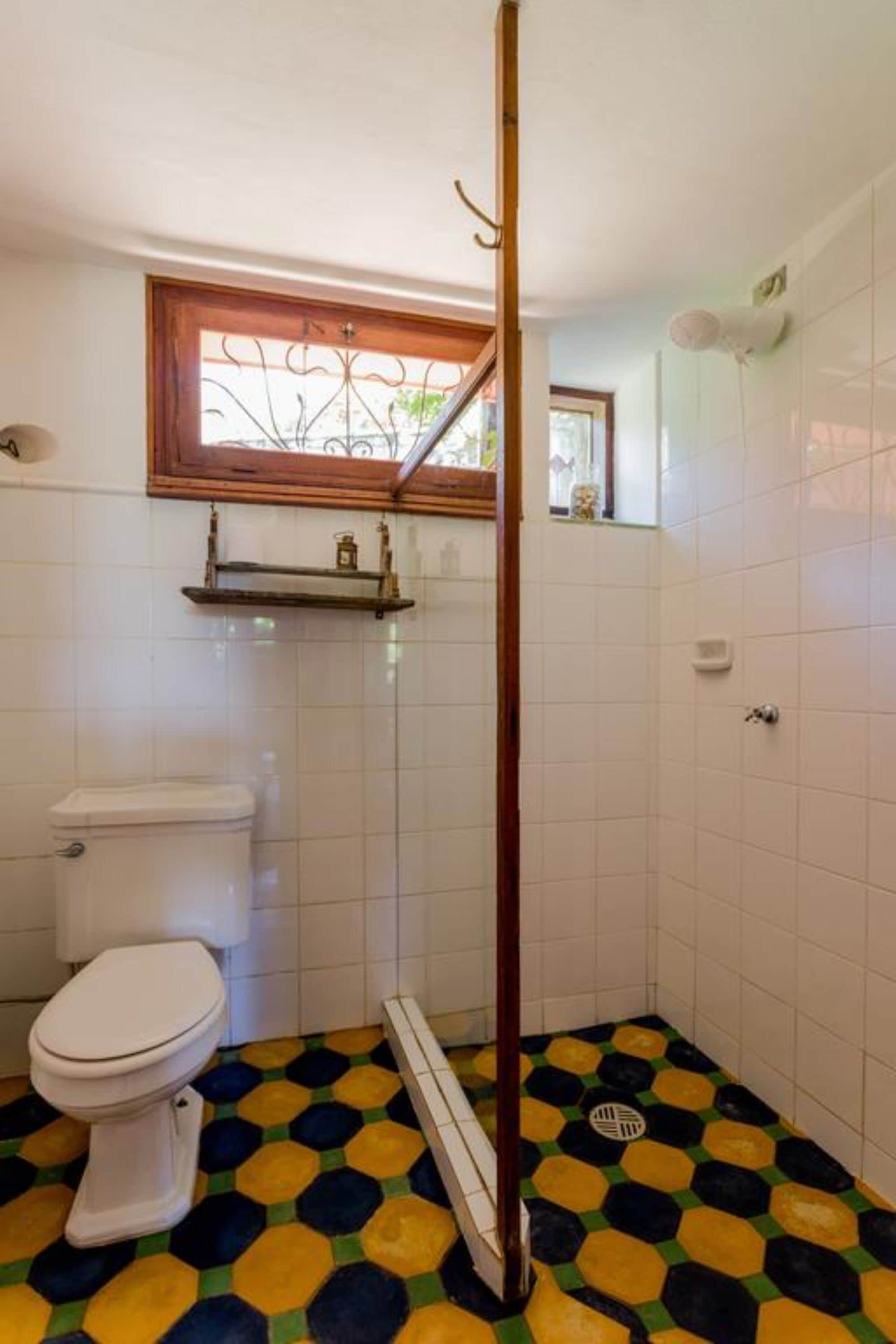 A bathroom with a toilet, a shower with a wooden door, and a tiled floor with a geometric pattern.