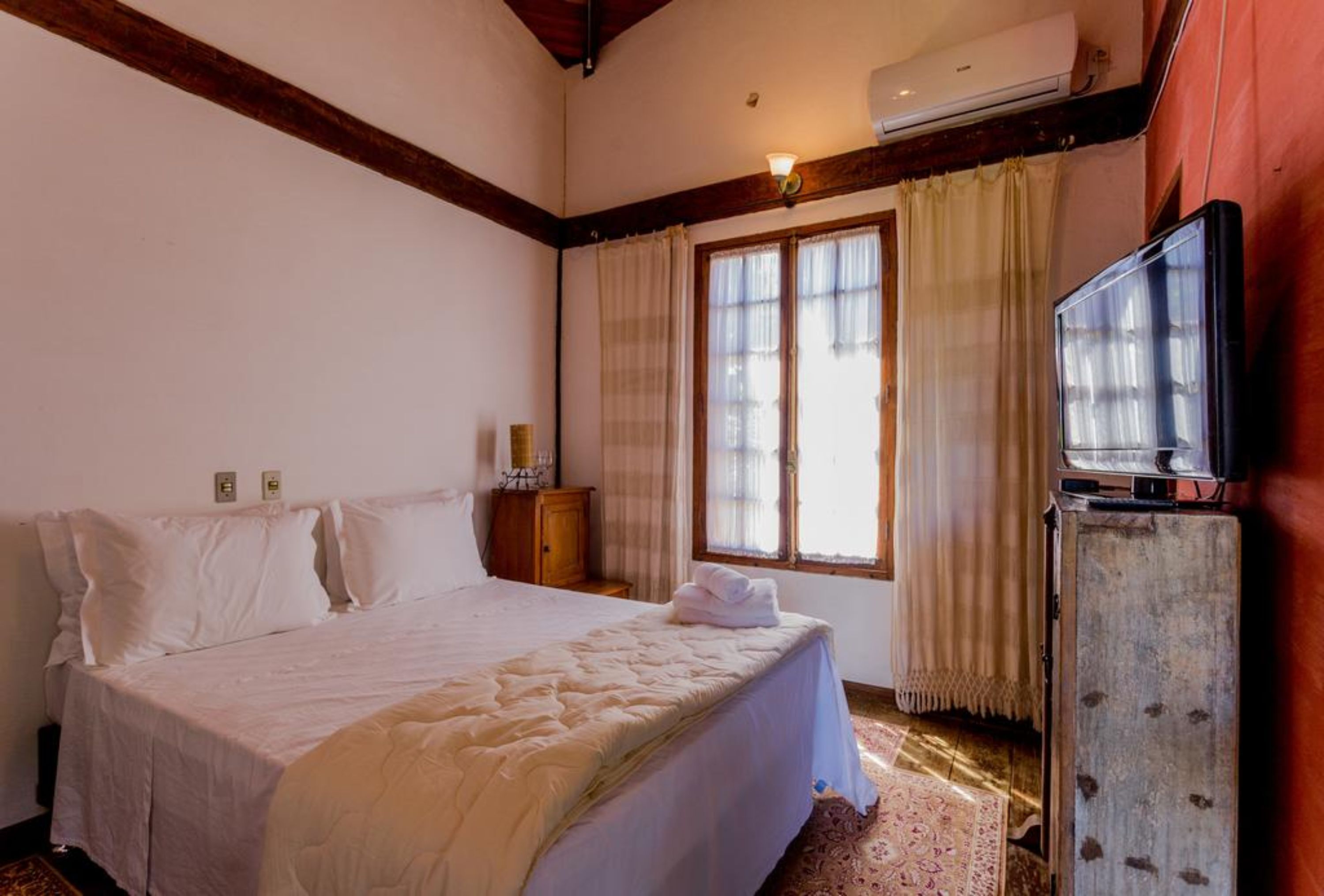 Un dormitorio con una cama grande, un cabecero de madera, un televisor sobre un mueble de madera y una ventana con cortinas.