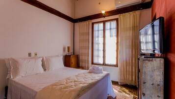 Un dormitorio con una cama grande, un cabecero de madera, un televisor sobre un mueble de madera y una ventana con cortinas.