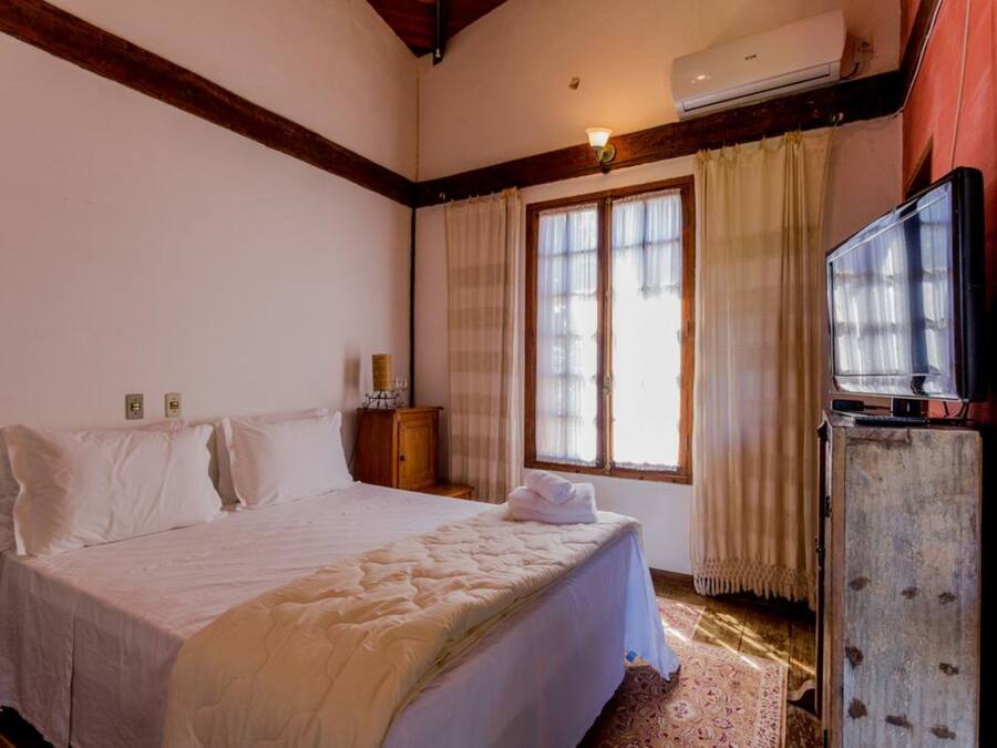 Un dormitorio con una cama grande, un cabecero de madera, un televisor sobre un mueble de madera y una ventana con cortinas.