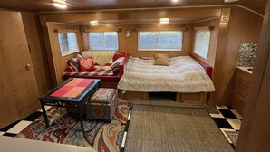 A compact RV interior with a sofa, a bed, a small table, and a patterned rug. - Meet the Ruby! (Inverness)