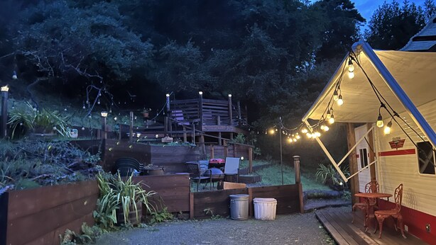 A campsite with a wooden deck, a covered seating area, and string lights. - Meet the Ruby! (Inverness)