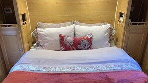 A cozy bed with striped bedding and floral pillows, a red blanket, and a wooden headboard. - Meet the Ruby! (Inverness)