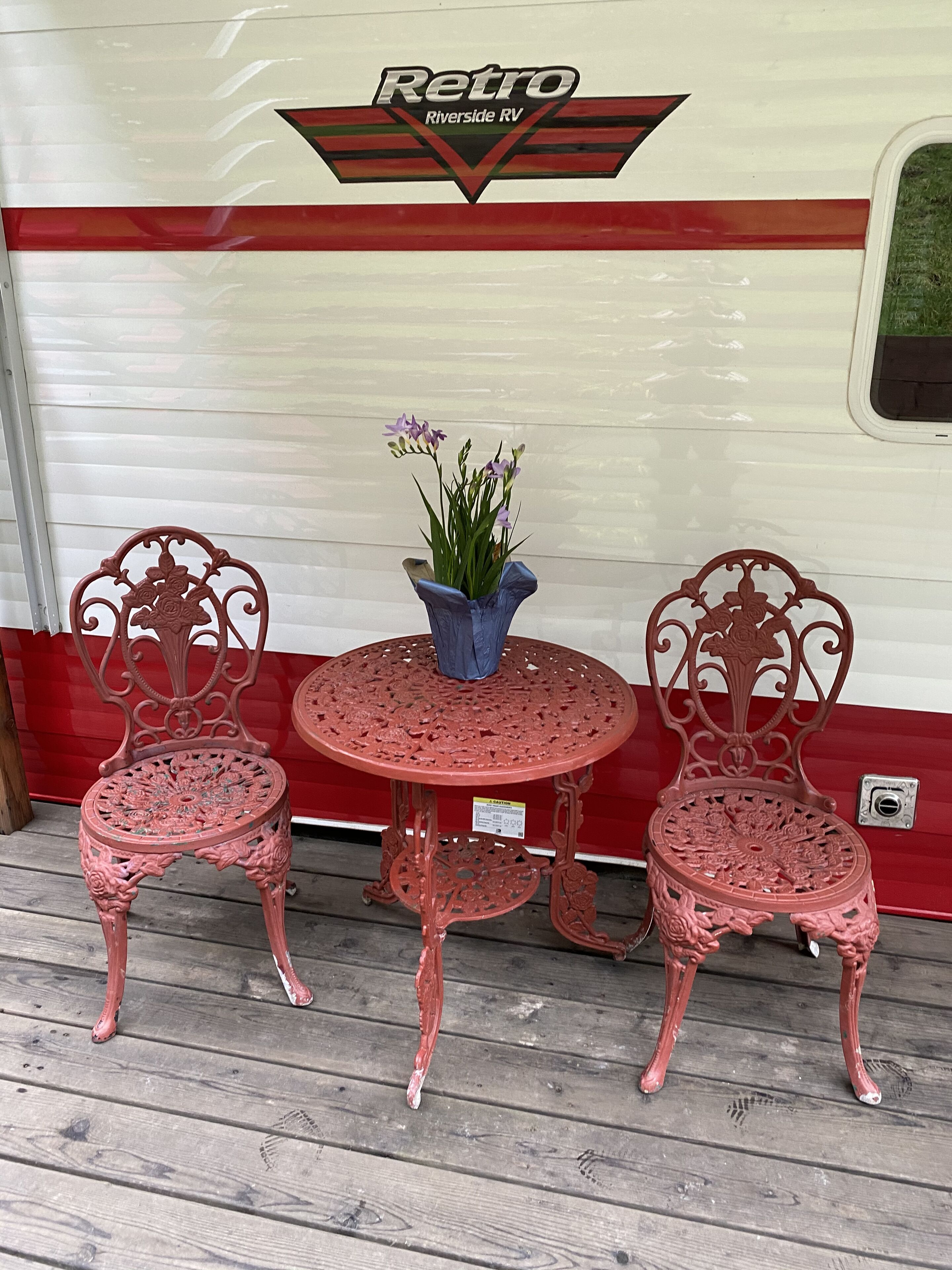 A red metal table and chairs set against a white RV with a 'Retro Riverside RV' logo.