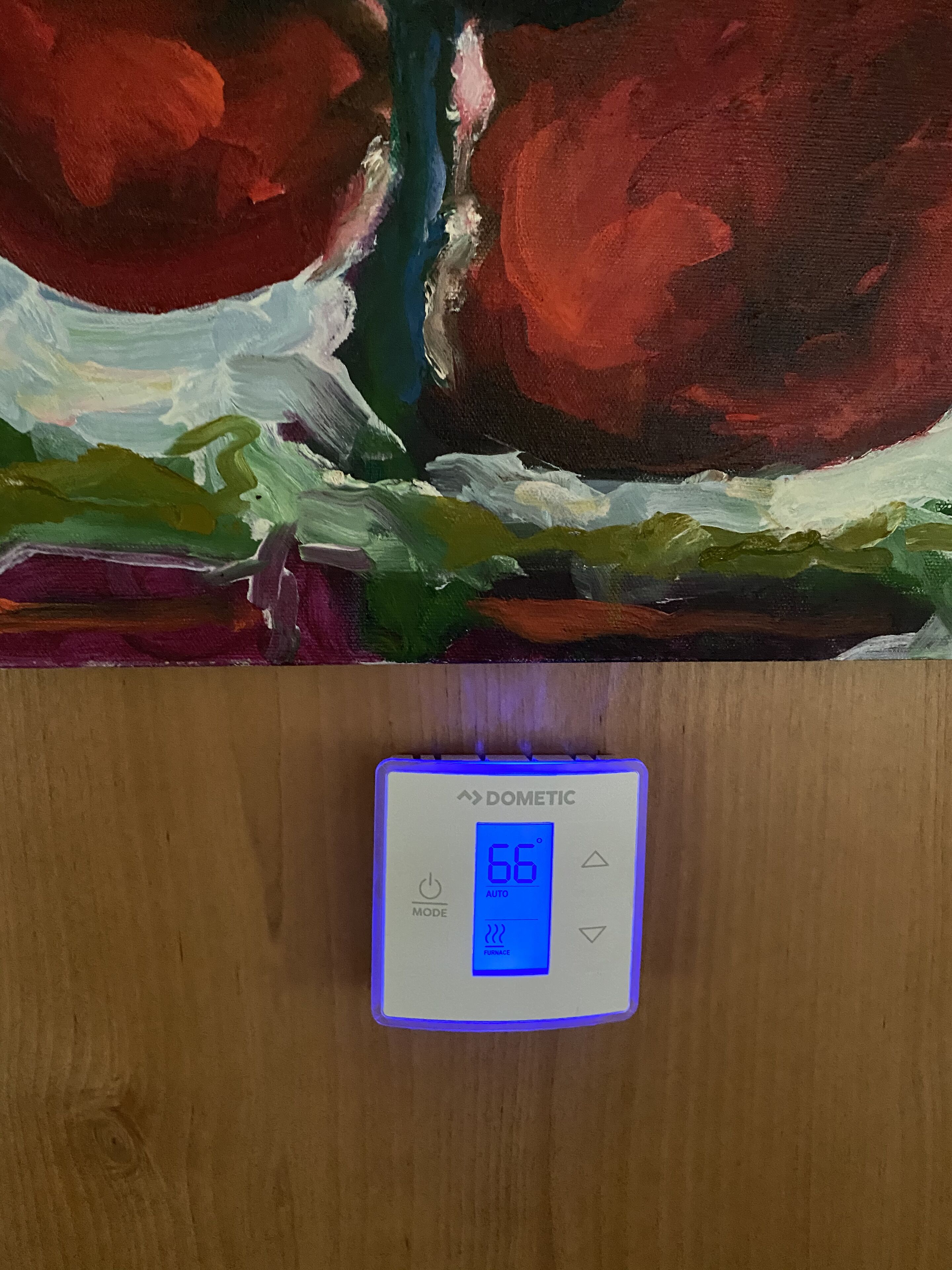 A thermostat displaying 66 degrees Fahrenheit in AUTO mode, mounted on a wooden surface.