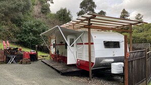 A white RV with a red stripe, a covered porch, and a small table with chairs. - Meet the Ruby! (Inverness)
