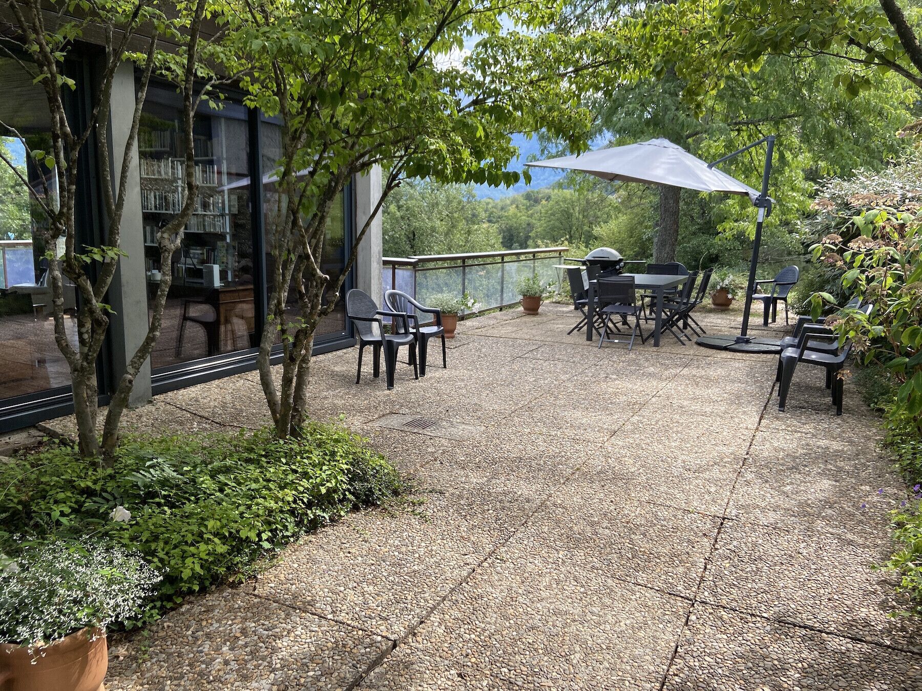 Een terras met tuinmeubilair, een barbecue en uitzicht op een gebouw met grote ramen.