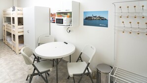 Een kamer met een stapelbed, een magnetron, een tafel met stoelen, een afbeelding van Alcatraz en een haken systeem aan de muur.