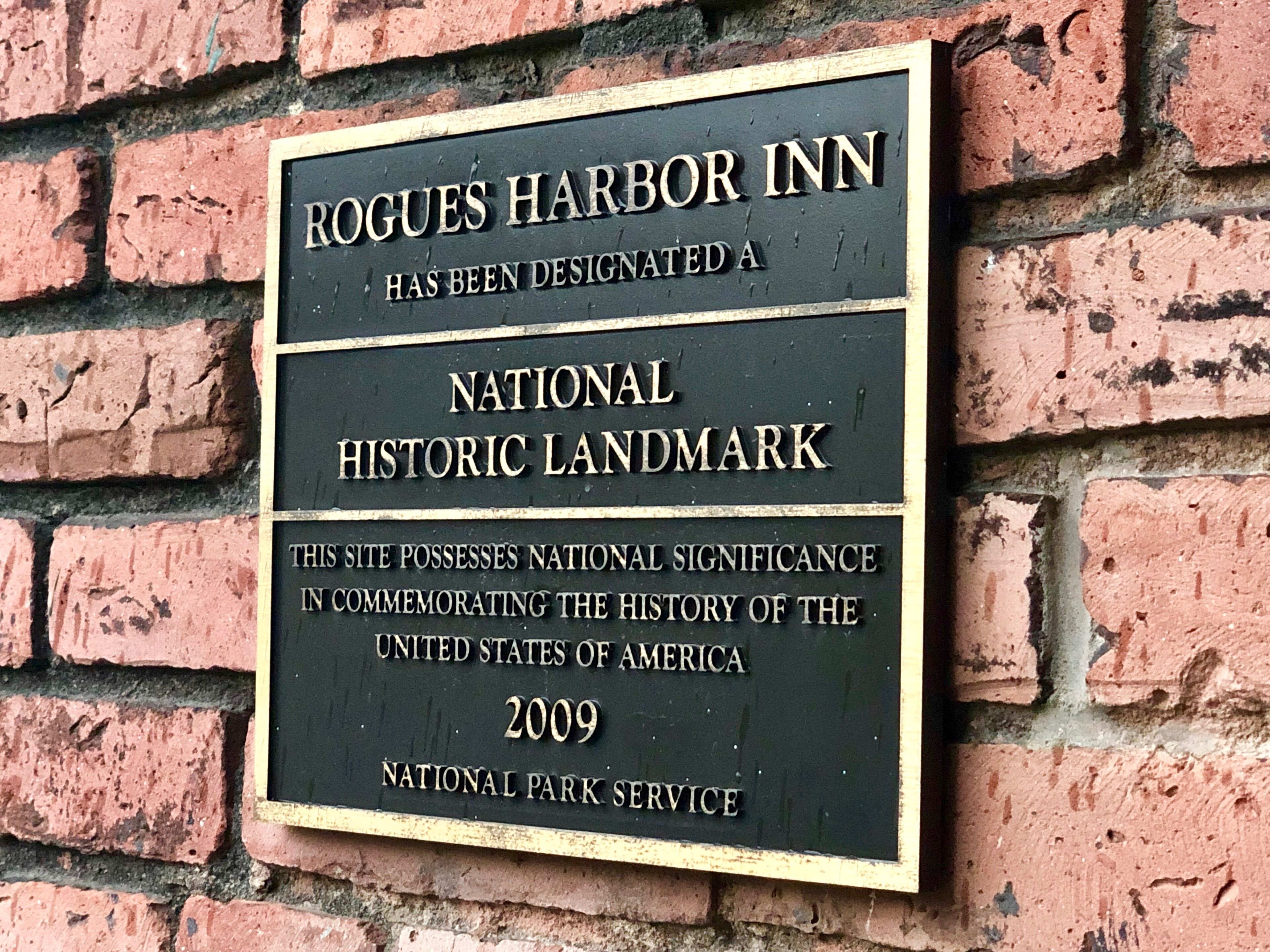 A sign indicating that the ROGUES HARBOR INN has been designated a NATIONAL HISTORIC LANDMARK.