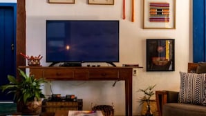 A living room with a TV, wooden furniture, and various decorative items on the walls and coffee table. - Ilhabela Homestay (Ilhabela)